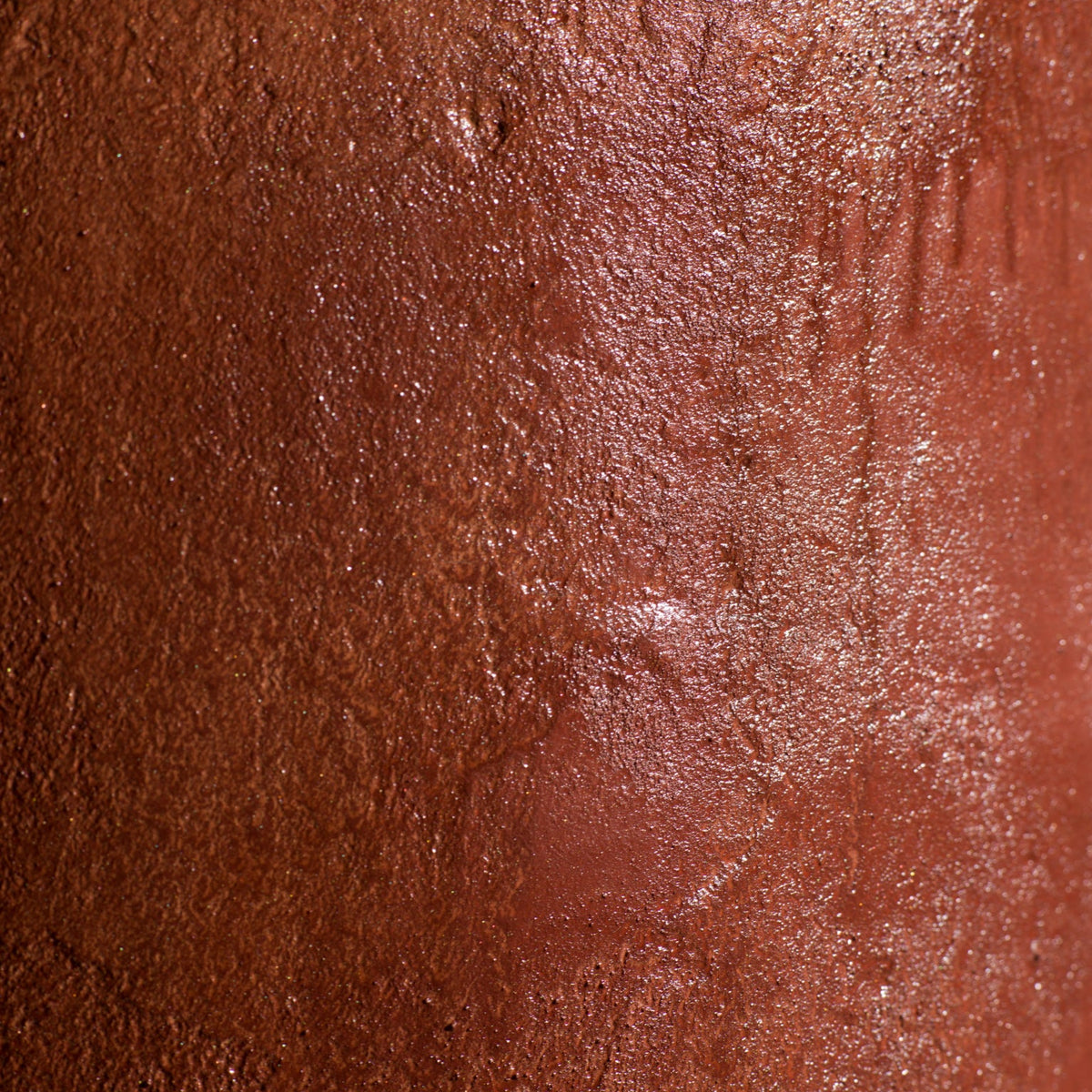 A close-up of a cylindrical micro-cement stool in a bloody orange color, with a rough-textured, glossy finish, displayed on a white pedestal against a neutral grey wall.