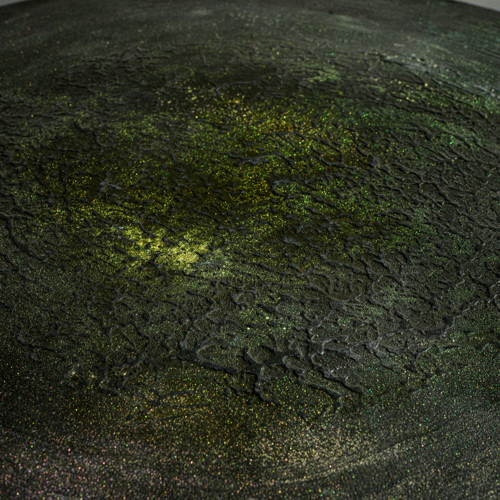 A close-up of a handmade round black concrete low table with a cylindrical pedestal base.