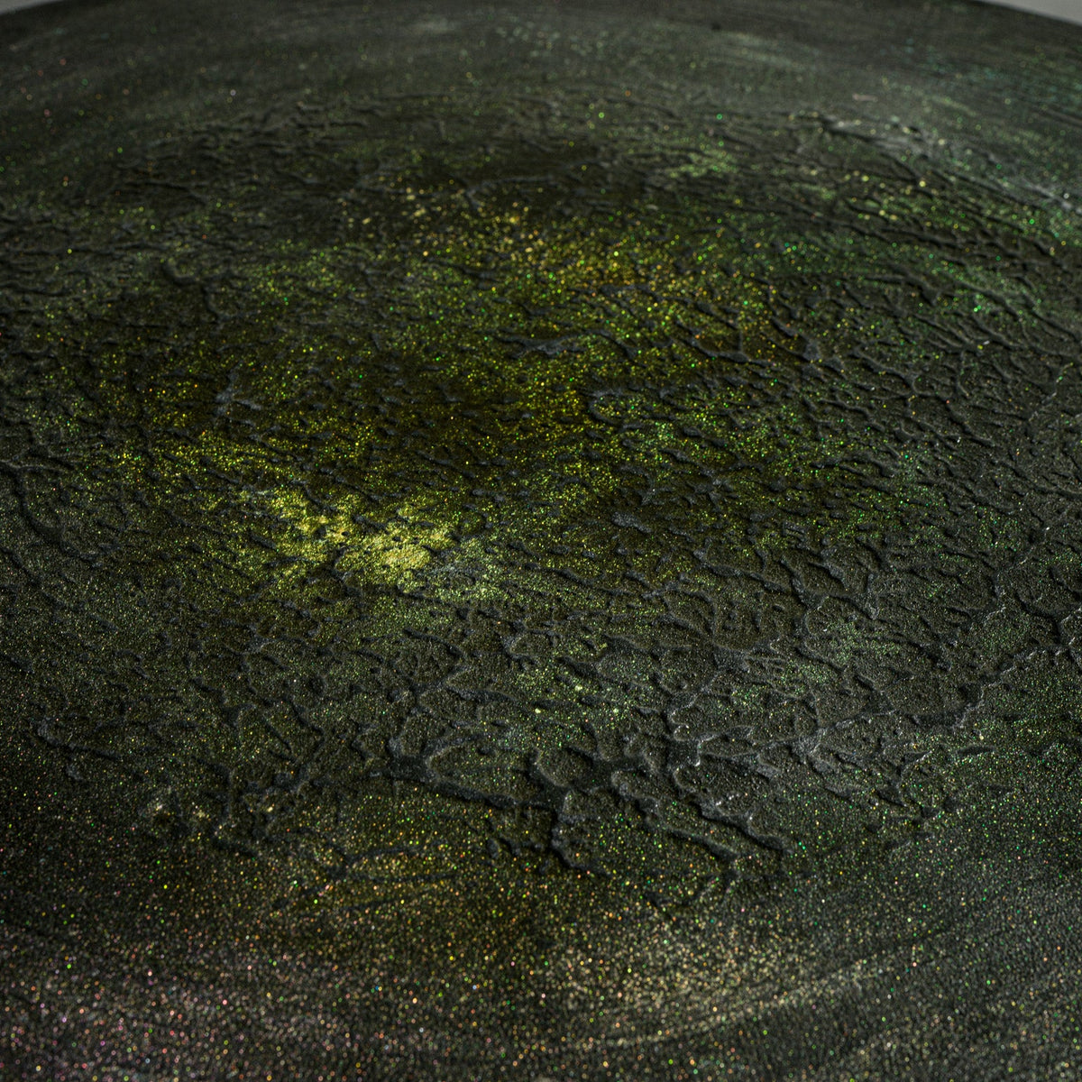 A close-up of a handmade round black concrete low table with a cylindrical pedestal base.