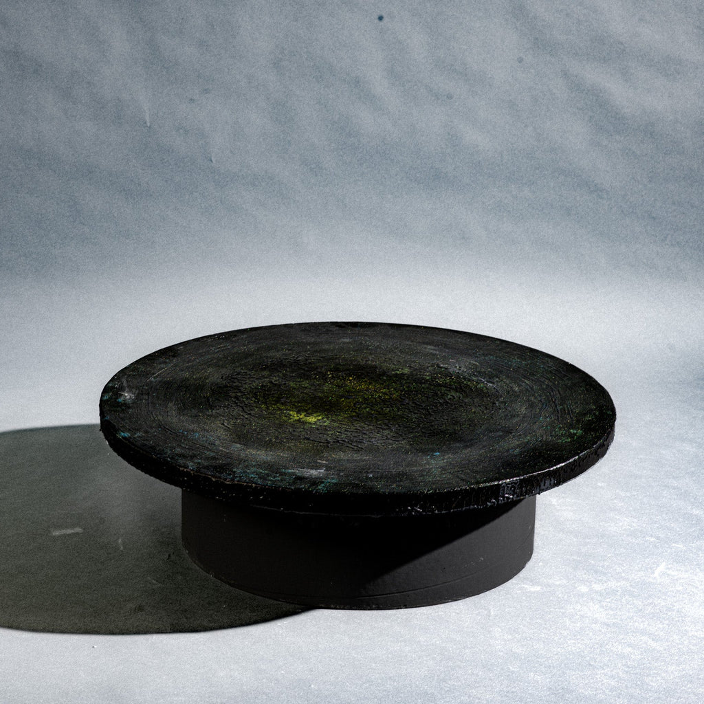 A handmade round black concrete low table with a cylindrical pedestal base.