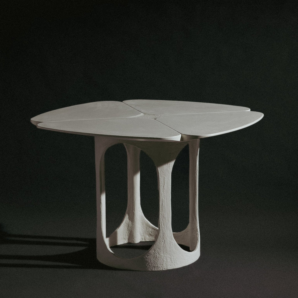A handmade sculptural, feminine table with a four-petal clover-shaped top and a textured, organic-shaped base, shown on a dark studio background.