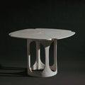 A handmade sculptural, feminine table with a four-petal clover-shaped top and a textured, organic-shaped base, shown on a dark studio background.