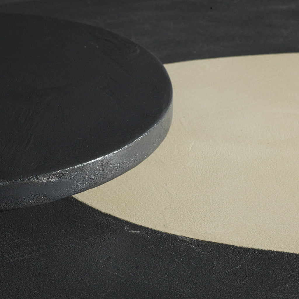 A close-up of a dark charcoal grey round bread plate resting on table with a dark gray and a large cream-colored top.