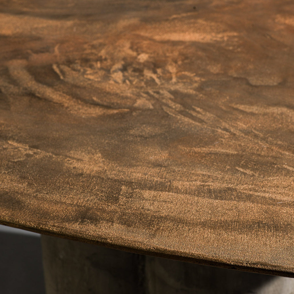 A close-up of a handmade triangle-shaped dinning table with a bronze top and a triple round column base with dark gray stone texture, set against a dark gray studio background.