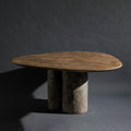 A handmade triangle-shaped dinning table with a bronze top and a triple round column base with dark gray stone texture, set against a dark gray studio background.