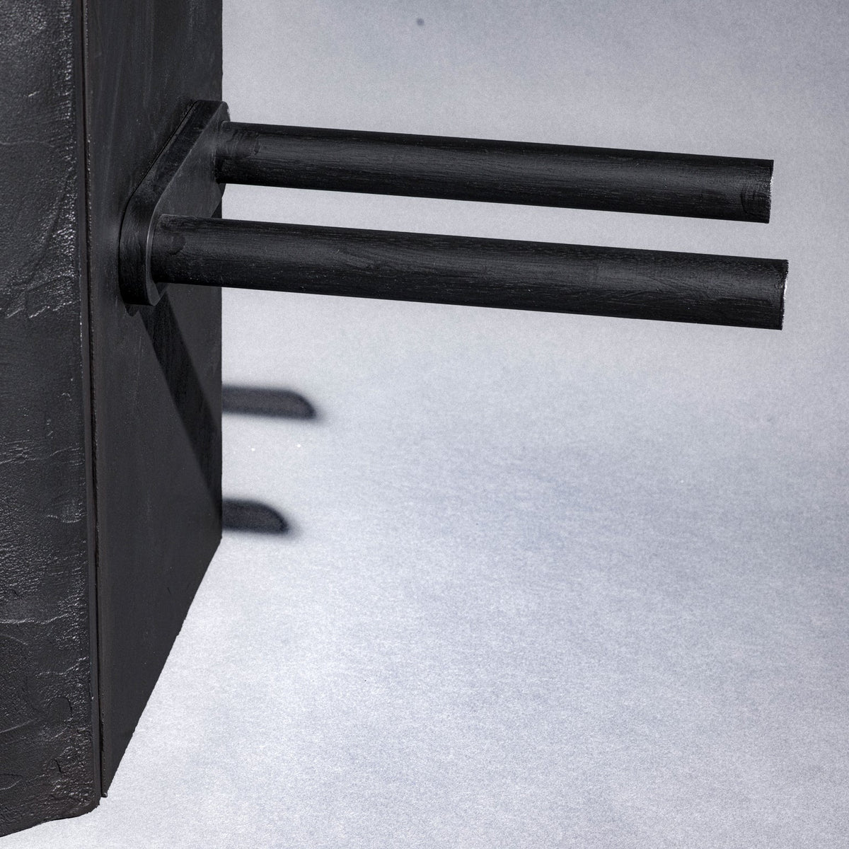 A close-up of a black closet bottom part  cylindrical product with two parallel cylindrical protrusions extending from the side, shown against a light gray background.