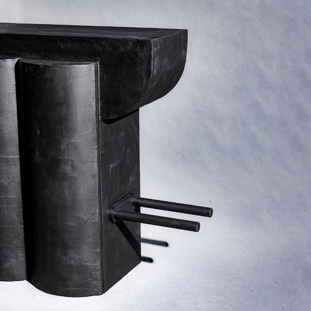 A close-up studio shot of a dark sculptural closet, showing a thick rectangular top and cylindrical side front doors with the shape of an Aztec sculpture.