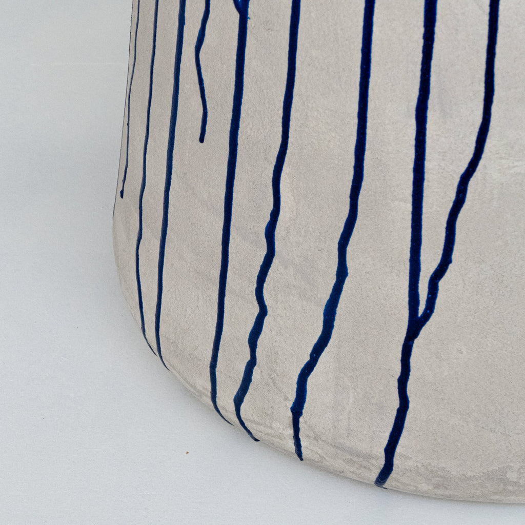 Close-up of a textured light grey concrete finished stool with navy blue vertical drip-like lines.