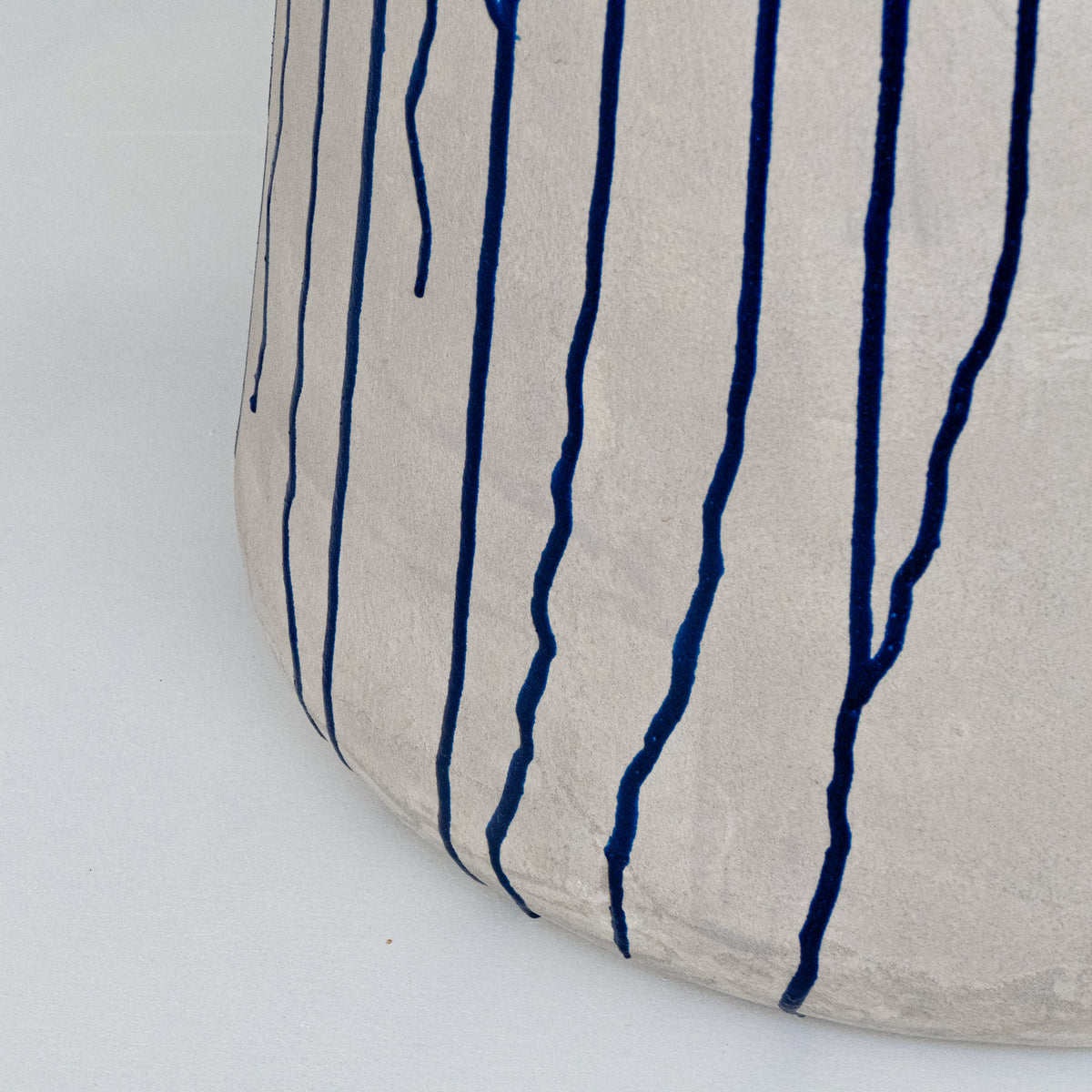 Close-up of a textured light grey concrete finished stool with navy blue vertical drip-like lines.