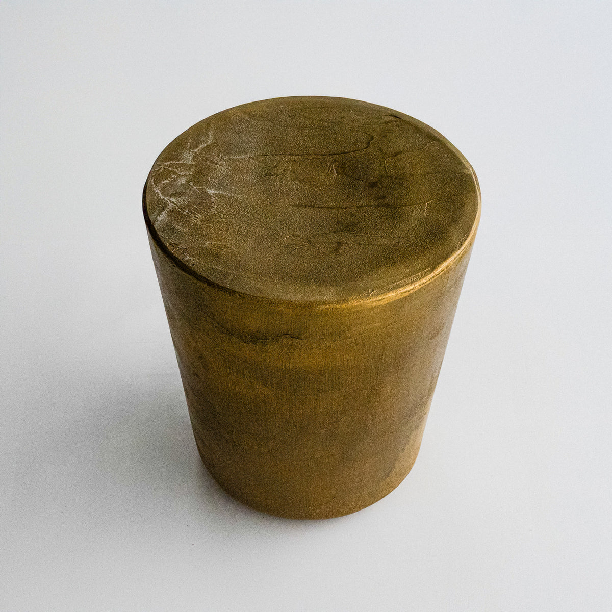 A cylindrical, metallic gold-finished Van Roosberg stool with a rough, brushed texture, displayed on a light gray concrete pedestal against a neutral off-white background.