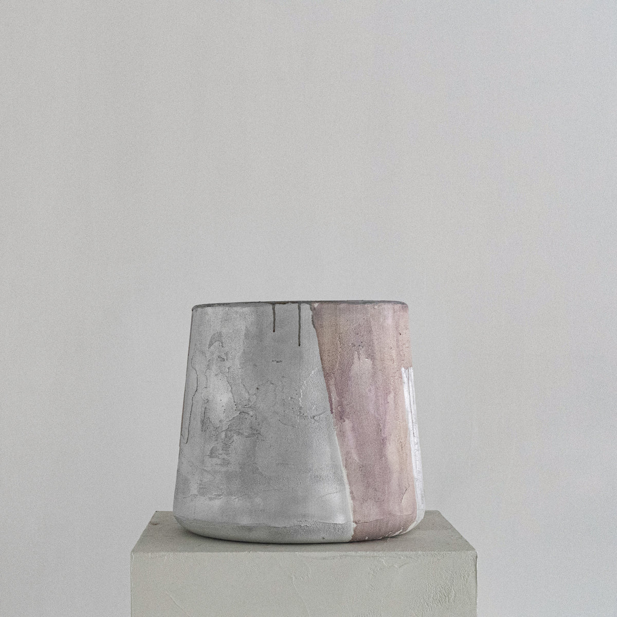 A handmade Van Roosberg sculptural stool with a tapered shape, featuring horizontal bands of textured dusty rose, metallic silver, and earthy brown glaze finishing. Displayed on a minimalist concrete pedestal against a neutral gray background.