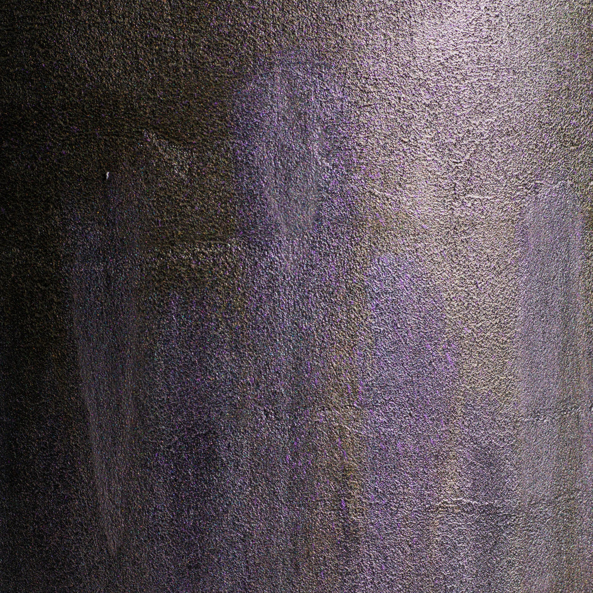 A close-up of a textured surface with a mottled pattern of dark gray, black, and muted purple.